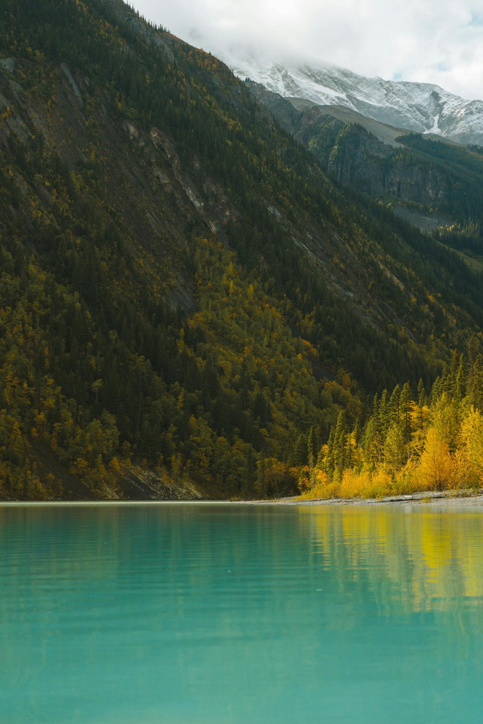 Serene autumn landscape with alpine lake and majestic mountains under cloudy sky.