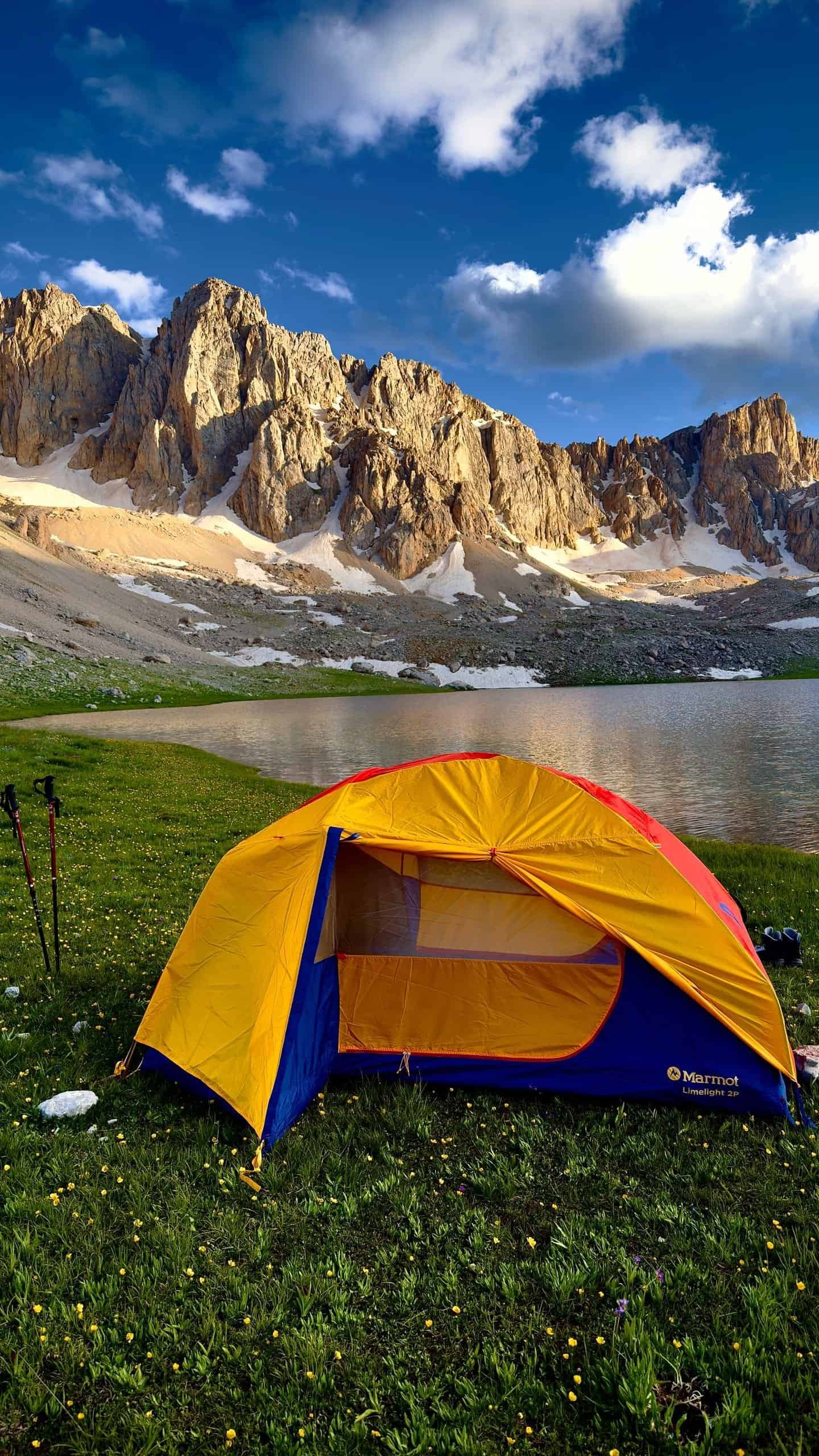 Camping tent by a serene mountain lake with peaks at sunset.